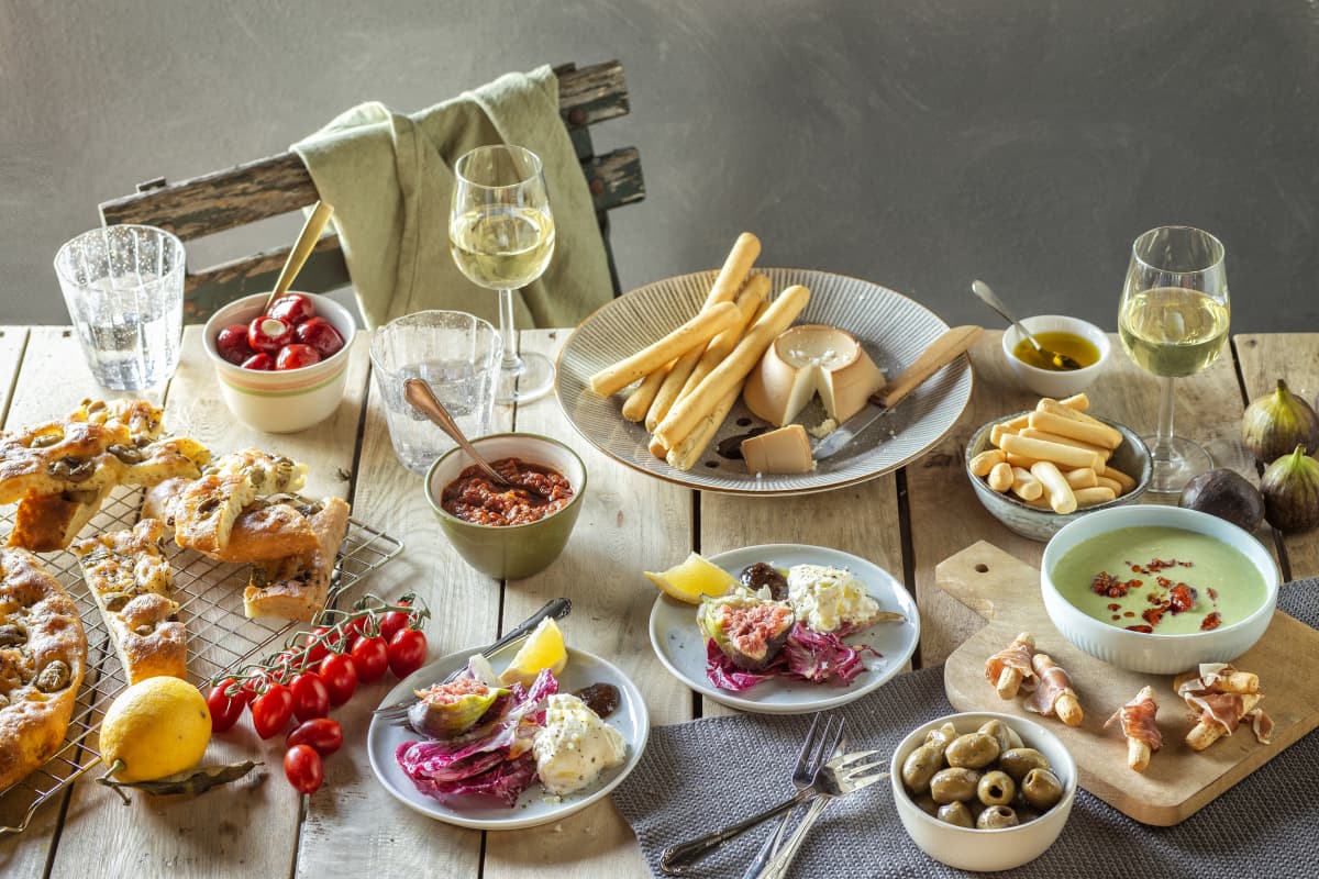 Tafel met witte wijn, soepstengels, gevulde pepers, tapenade, vijgen, cherrytomaten, focaccia, olijven, olie